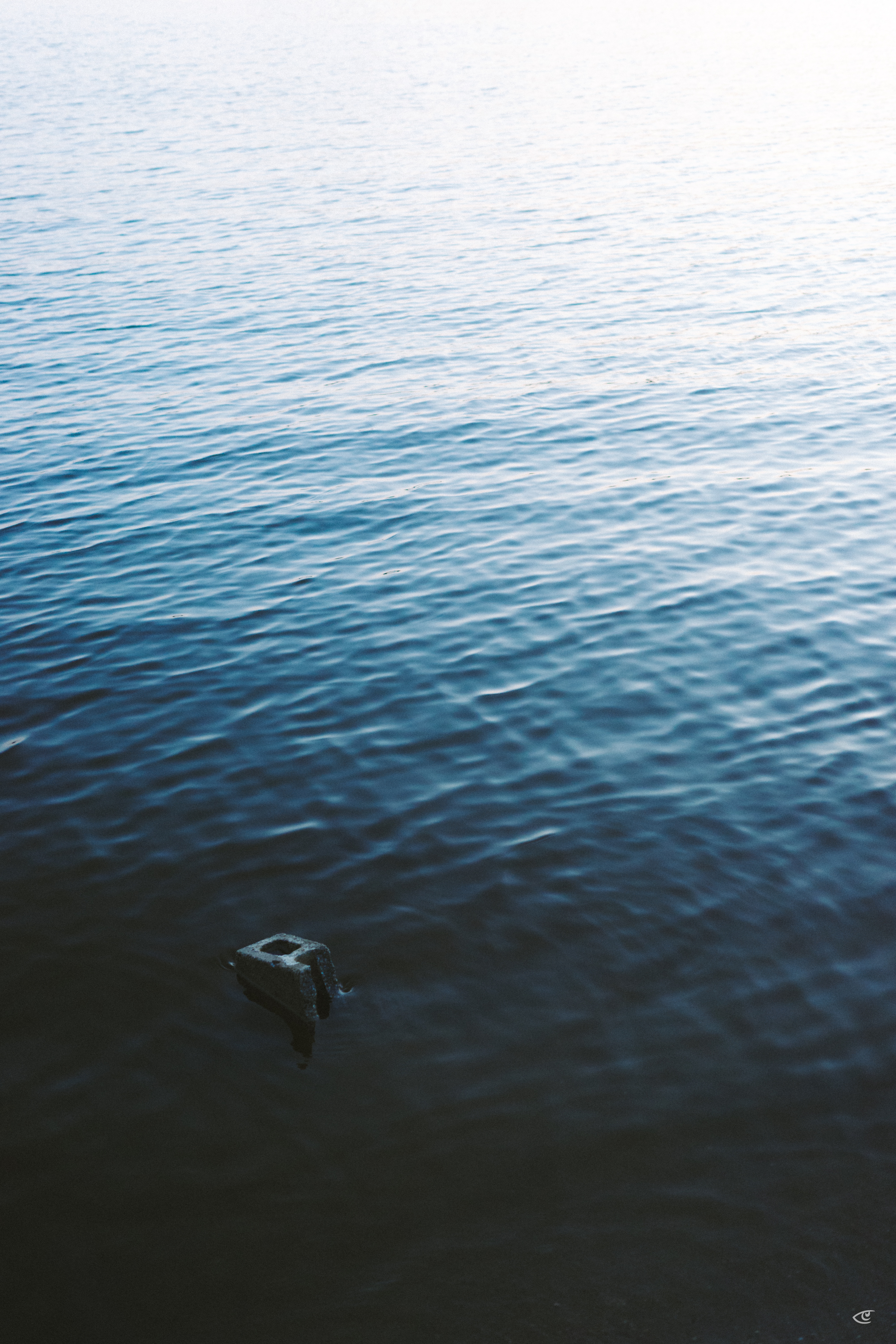 Rippling blue water fills the frame, fading to bright glare near the top; a small dark metal bracket or mooring fixture protrudes from the water near the lower left.