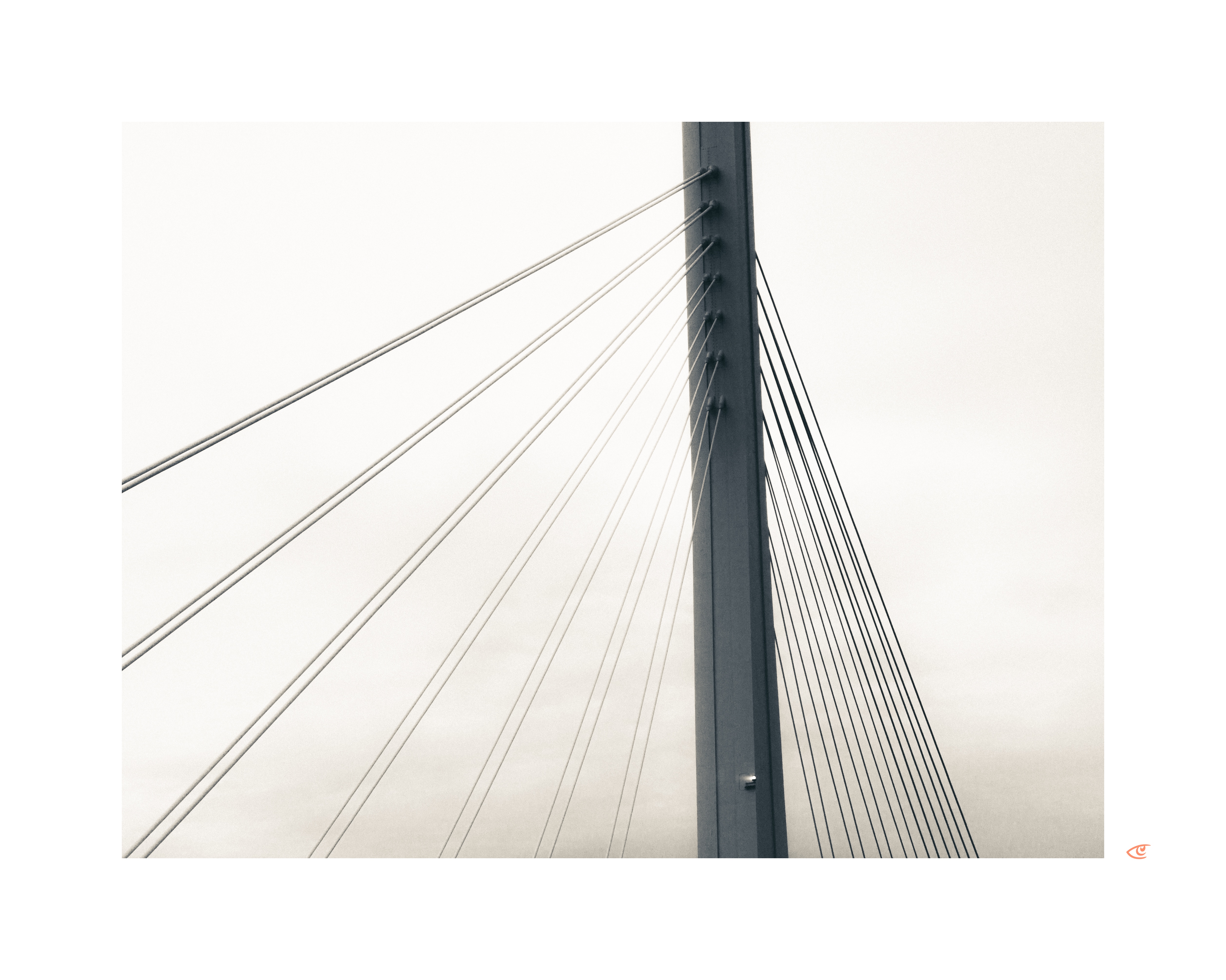 Central vertical pylon of a cable-stayed bridge with multiple angled support cables extending left and right against an overcast sky.