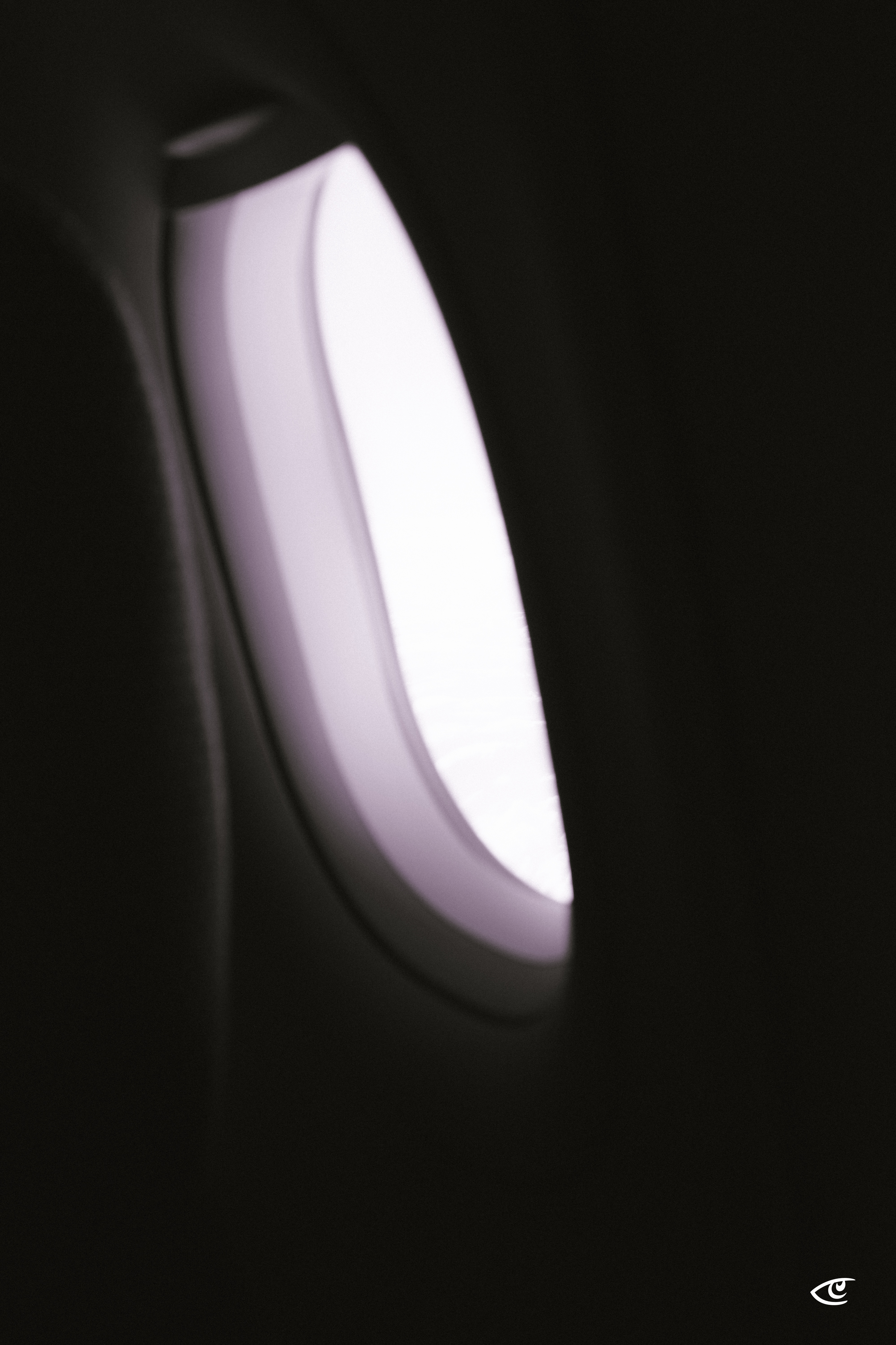 Close-up of an oval, white wall-mounted light fixture glowing against a dark background, positioned on the left side of the frame.