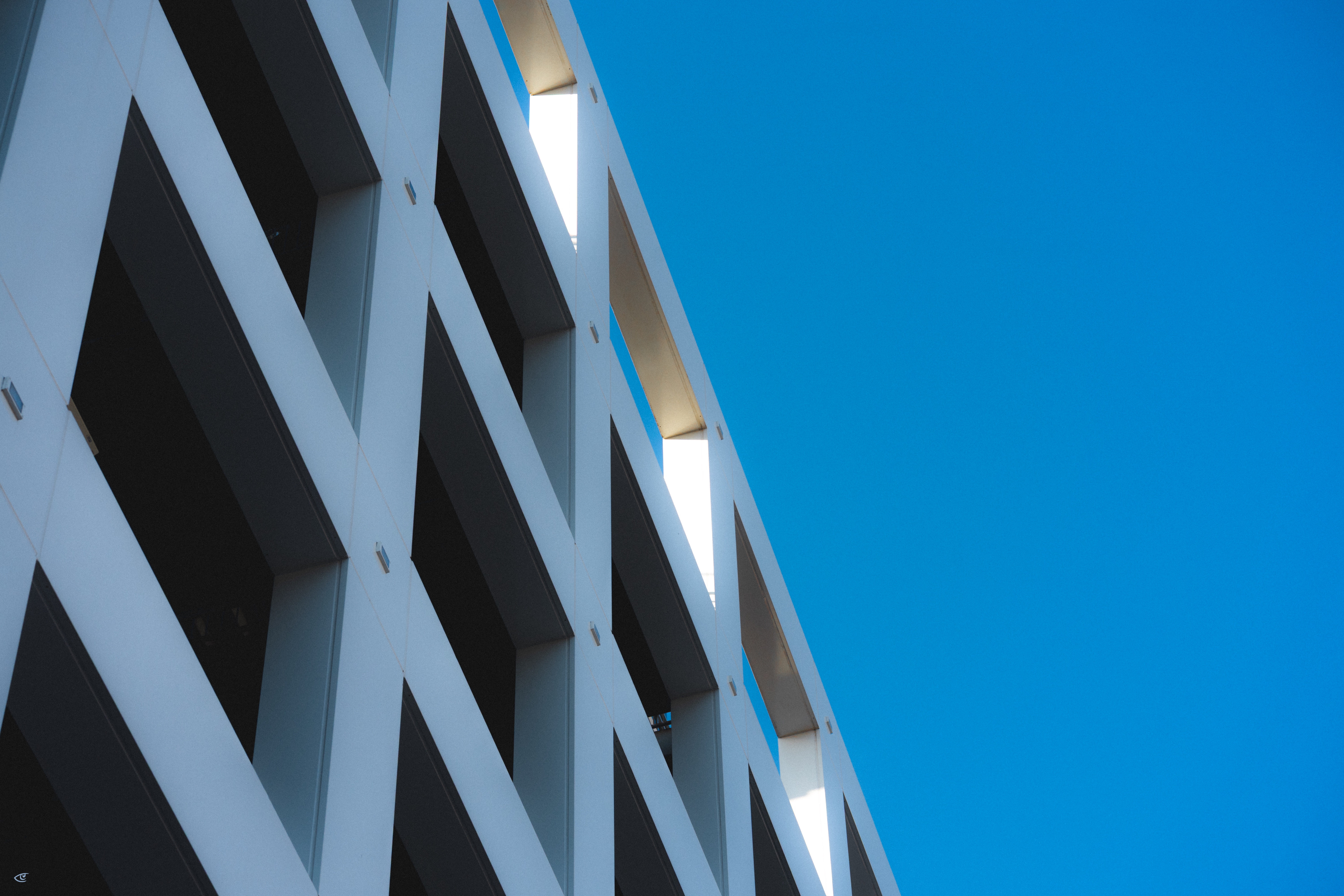 Upward angled view of a modern building facade with repeating square window openings and light-colored concrete, set against a clear blue sky.